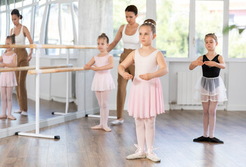 Fototapeta premium Female teacher conduct training, performs correction of pose in first position students. Girls engaged in ballet studio, perform repetitions of elements and tasks