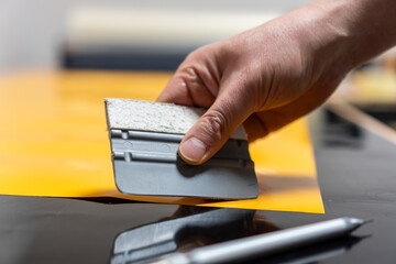 Detail of the hand of a person who makes stickers from foil. The man is holding a plastic spatula on the work table.