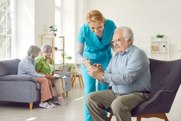 Positive caring kind smiling nurse, geriatric medicine caretaker providing senior man help with phone to support aged old during medical visit in retirement home, female doctor caregiving service 