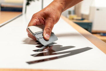 A hand holding a plastic squeegee during the production of foil advertising stickers. Preparation...