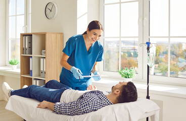 Friendly female nurse taking care of man in hospital. Happy young woman in scrubs holding...