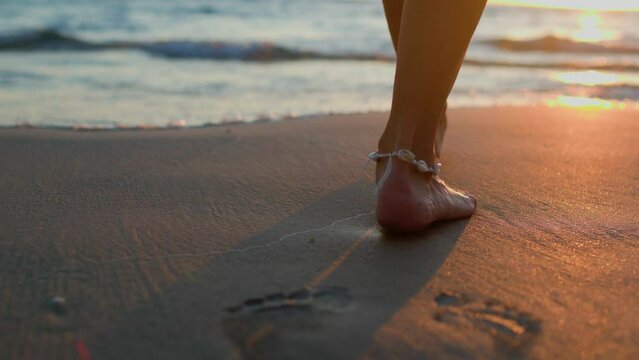 woman walks barefoot on the beach and leaves footprints in the sand. a girl goes into the sea. legs of a young beautiful tanned girl at sunset sun rays. travel and adventure. Summer mood.
