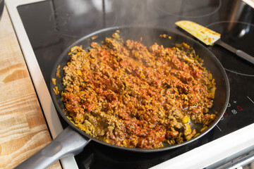  Minced meat with tomato sauce is fried in a frying pan in the kitchen. Homemade food concept.