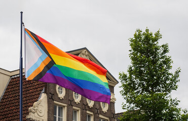 Amsterdam on Pride Month. Progress pride flag on a flagpole on background of an old dutch house. Amsterdam show their tolerance for the LGBTQ community and all deversitive people.