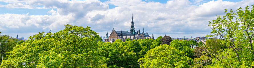 Obraz premium The Nordic Museums historic architecture stands out above vibrant, summertime foliage under a partly cloudy sky in Stockholm, Sweden.
