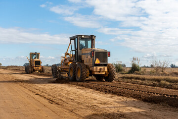 Maquinaria pesada niveladora trabajando en la construcción de una carretera de tierra bajo un...