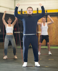 Sportive young man practicing with sports band in exercise room during weight training classes