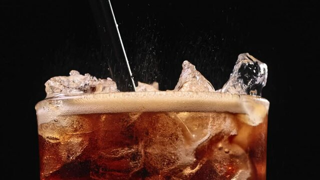Closeup of pouring cola drink with ice cubes. Fizzing cola with ice in glass. Refreshing tasty cola drink.