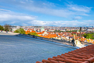A panoramic view over the red rooftops of Prague Lesser Town, with a scattering of tourists against the skyline under a spring bright sky. Prague, Czechia