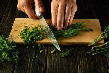 The chef cuts green fresh dill with a knife on a cutting board. Vegetarian menu concept for a...