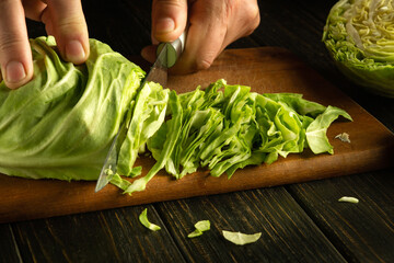 Preparing a salad from fresh cabbage. The hand of a cook with a knife cuts cabbage on a kitchen board for preparing a vegetarian dish.