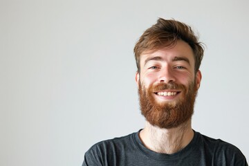 Fototapeta premium A headshot of a bearded young man with a genuine, friendly smile on a neutral background