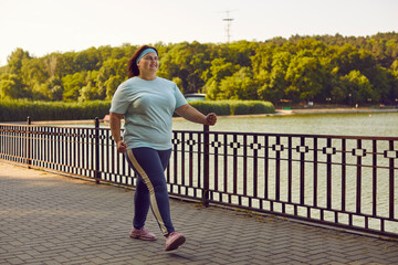 Overweight happy smiling fat woman having sport training in the summer city park walking outdoors....