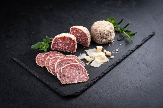 Traditionelle italienische Saltufo Salami mit Parmesan ummantelt und Tr&uuml;ffel serviert als Nahaufnahme auf einem schwarzen Design Tablet