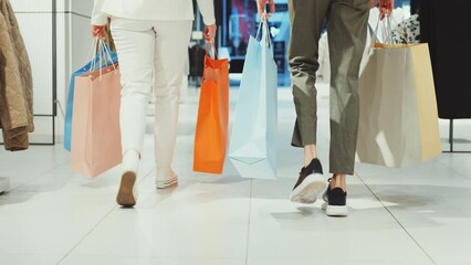 Couple walking through mall holding colorful shopping bags after successful purchases, enjoying day of shopping together. Focus on their legs and bags. Concept of retail therapy and consumer lifestyle - Powered by Adobe