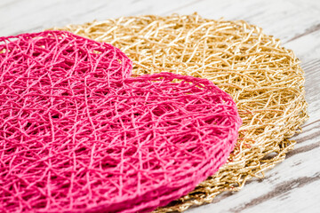 Pink and golden heart shaped mats with a textured surface on white wooden background.