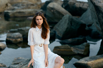 Serene ocean view young woman in elegant white dress relaxing on rocks by the sea
