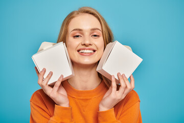A beautiful blonde woman holds two food boxes in front of her face, concealing her expression with...
