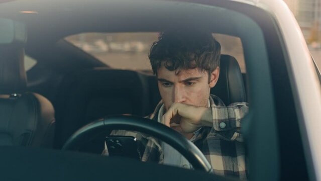 Displeased upset sad Caucasian man guy male driver car owner inside automobile on parking lot using mobile phone problem with smartphone read bad news frustrated anxious millennial driving auto city