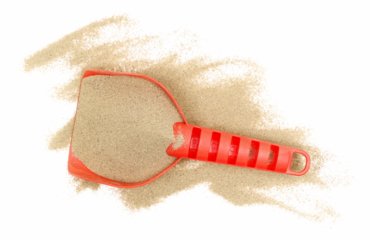 Red plastic shovel in sand, beach toy isolated on white, top view