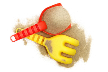 Red plastic shovel and rake in sand, beach toy isolated on white, top view