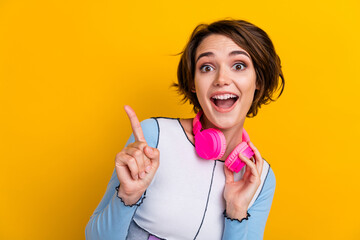 Photo of pretty impressed woman wear top listening music headphones pointing empty space isolated...
