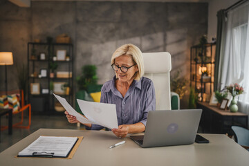 Mature senior woman work from home use laptop and hold documents