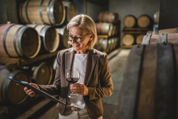 Mature senior woman stand in basement hold clipboard and glass of wine