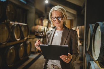 Mature senior woman stand in basement hold clipboard and glass of wine