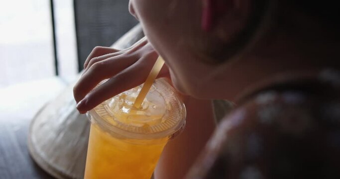 girl drinks freshly squeezed tangerine juice from a plastic glass. Convenient transplantation food delivery in hot weather in Vietnam.