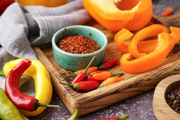 Wooden board with different fresh peppers and bowl of dried spices on dark background