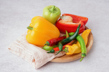 Wooden plate with different fresh peppers on white background