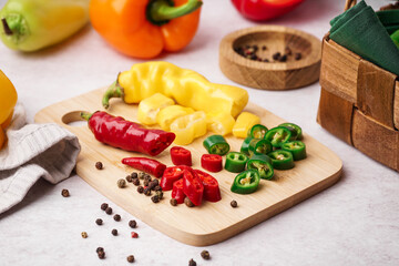 Wooden board with cut chili peppers and peppercorn on white background