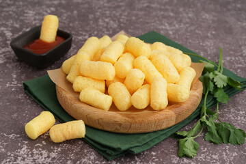 Wooden plate with tasty salty corn sticks and ketchup on grunge background, closeup