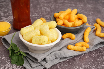 Bowls with tasty salty corn sticks and sauce on grunge background, closeup