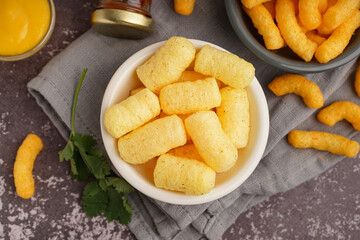 Bowls with tasty salty corn sticks and sauce on grunge background, closeup
