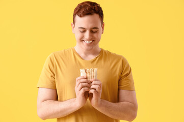 Young happy man smiling and holding doner kebab on yellow background
