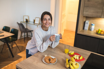 Dark-haired caucasian woman at the kitchen looking relaxed and contented