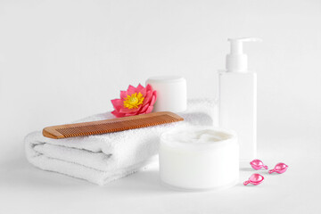 Jars of hair mask with bottle of cosmetic product, towel and comb on white background