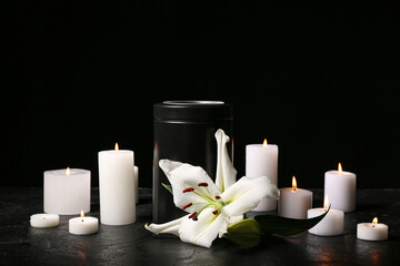 White flower, mortuary urn and candles on black background