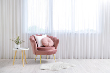 Interior of living room with pink armchair, magazine, cushions, houseplant and coffee table