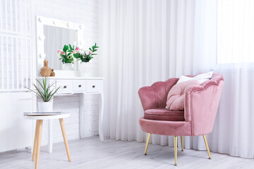 Interior of living room with pink armchair, chest of drawers, houseplant and coffee table