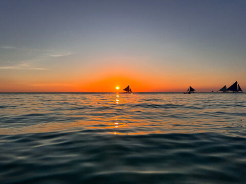 Sailing boats under beautiful orange sunset at Boracay Island of Philippines