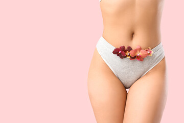 Young woman in panties with beautiful orchid flowers on pink background