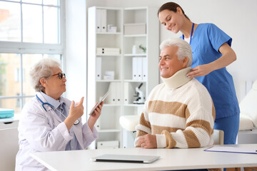 Senior doctor and nurse putting cervical collar on mature man in clinic