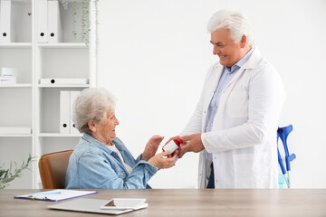 Obraz premium Senior woman taking pill bottle from doctor in clinic