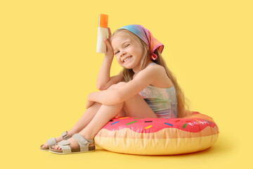 Cute little girl with sunscreen cream sitting on swim ring against yellow background