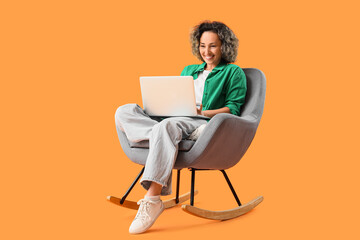Mature woman using laptop in rocking armchair on orange background