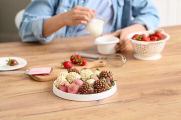 Beautiful young woman preparing chocolate covered strawberries at home