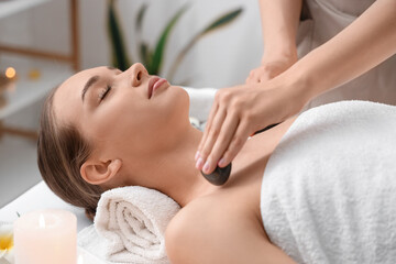 Young woman getting massage with stones in spa salon, closeup